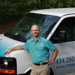 Tidy Guy standing by his work van on a sunny day, wearing a uniform and smiling