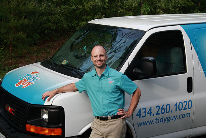 Tidy Guy standing by his work van on a sunny day, wearing a uniform and smiling. 